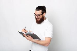 homem barbudo fazendo anotações na agenda ou planejador sobre fundo branco foto