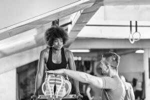 mulher negra fazendo exercício de barras paralelas com treinador foto