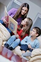 jovem mãe brinca com seus filhos em casa e lendo livro foto