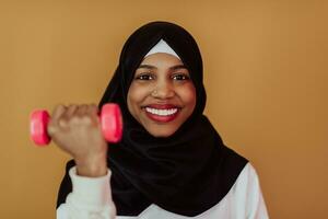 africano americano muçulmano mulher promove uma saudável vida, segurando halteres dentro dela mãos foto