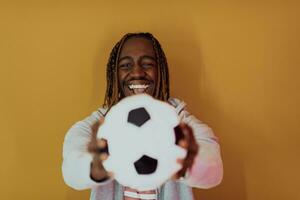 africano americano homem posando em uma amarelo fundo enquanto segurando uma futebol bola foto