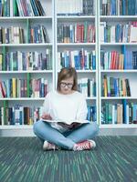 aluna menina lendo livro dentro biblioteca foto