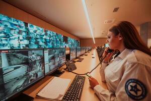 fêmea segurança guarda operador falando em a telefone enquanto trabalhando às posto de trabalho com múltiplo monitores segurança guardas trabalhando em múltiplo monitores foto