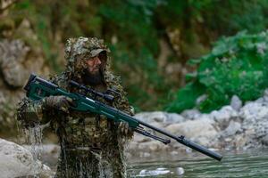 uma militares homem ou airsoft jogador dentro uma camuflar terno esgueirar-se a rio e mira a partir de uma Franco atirador rifle para a lado ou para alvo. foto