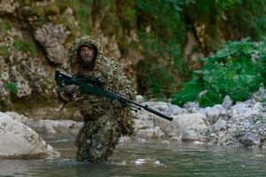 uma militares homem ou airsoft jogador dentro uma camuflar terno esgueirar-se a rio e mira a partir de uma Franco atirador rifle para a lado ou para alvo. foto