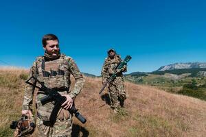 uma Franco atirador equipe pelotão do soldados é indo disfarçado. Franco atirador assistente e equipe líder caminhando e visando dentro natureza com amarelo Relva e azul céu. tático camuflar uniforme. foto