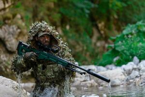 uma militares homem ou airsoft jogador dentro uma camuflar terno esgueirar-se a rio e mira a partir de uma Franco atirador rifle para a lado ou para alvo. foto