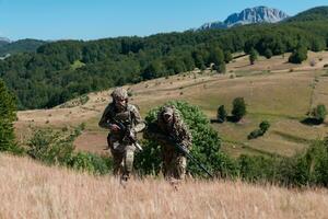 uma Franco atirador equipe pelotão do soldados é indo disfarçado. Franco atirador assistente e equipe líder caminhando e visando dentro natureza com amarelo Relva e azul céu. tático camuflar uniforme. foto