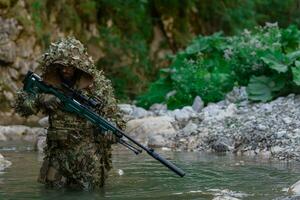 uma militares homem ou airsoft jogador dentro uma camuflar terno esgueirar-se a rio e mira a partir de uma Franco atirador rifle para a lado ou para alvo. foto