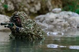 uma militares homem ou airsoft jogador dentro uma camuflar terno esgueirar-se a rio e mira a partir de uma Franco atirador rifle para a lado ou para alvo. foto