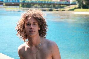 retrato do uma jovem adolescente Garoto com encaracolado molhado cabelo perto a rio tendo Diversão com amigos às uma verão Festa. foto