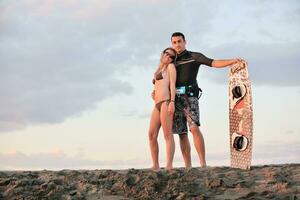 casal de surf posando na praia ao pôr do sol foto