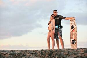 casal de surf posando na praia ao pôr do sol foto