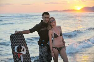 casal de surf posando na praia ao pôr do sol foto