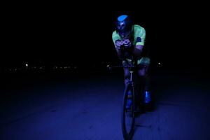 atleta de triatlo andando de bicicleta rápido à noite foto