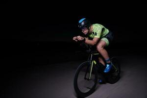 atleta de triatlo andando de bicicleta rápido à noite foto