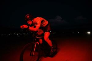 atleta de triatlo andando de bicicleta rápido à noite foto