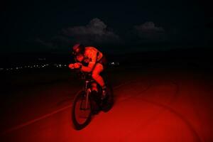 atleta de triatlo andando de bicicleta rápido à noite foto