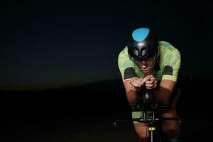 atleta de triatlo andando de bicicleta rápido à noite foto