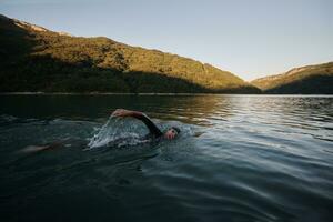 atleta de triatlo nadando no lago ao nascer do sol vestindo roupa de mergulho foto