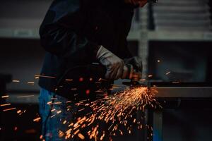 interior da fábrica de engenharia da indústria pesada com trabalhador industrial usando rebarbadora e cortando um tubo de metal. empreiteiro em uniformes de segurança e fabricação de capacetes de estruturas metálicas. foto