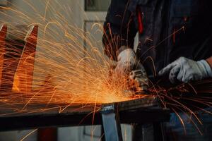 interior da fábrica de engenharia da indústria pesada com trabalhador industrial usando rebarbadora e cortando um tubo de metal. empreiteiro em uniformes de segurança e fabricação de capacetes de estruturas metálicas. foto