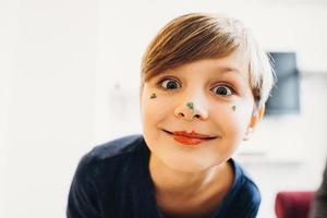 um menino fofo com o rosto pintado de palhaço com cor creme comestível foto