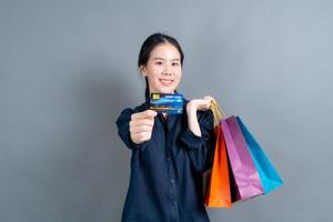 linda mulher asiática com sacolas de compras e apresentando cartão de crédito foto