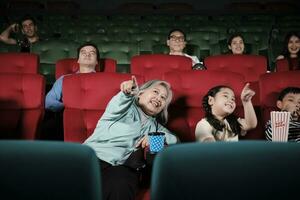 ásia família audiências apreciar assistindo cinema juntos às filme teatros. avó e crianças ter interior entretenimento estilo de vida com filme arte shows, feliz e alegre com Pipoca e uma sorriso. foto
