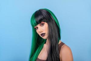 Mulher bonita usando meia peruca preta colorida verde contra o azul foto