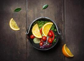 Salada de legumes fresca com laranja na frigideira sobre fundo de madeira foto