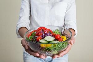mãos de mulher bonita segurando uma tigela grande de salada vegetariana fresca. foto
