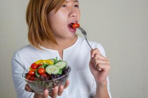 linda mulher em pé segurando uma tigela de salada e comendo alguns vegetais foto