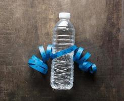 garrafa de plástico de água com fita métrica sobre o fundo de madeira foto
