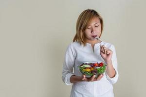 linda mulher em pé segurando uma tigela de salada e comendo alguns vegetais