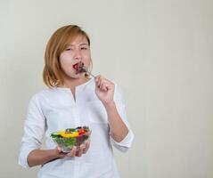 linda mulher em pé segurando uma tigela de salada e comendo alguns vegetais foto