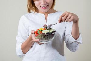 linda mulher em pé segurando uma tigela de salada e comendo alguns vegetais foto