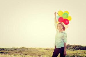 mulher em pé segurando balões coloridos no campo e sorridente foto