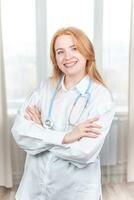 médico conceito. sorridente enfermeira com suspensórios e uma estetoscópio dentro dela mão. feliz e rindo fêmea médico dentro uma branco casaco posando às a Câmera. hospital trabalhador foto