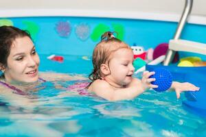 feliz mãe ensina dela pequeno filha para nadar dentro a piscina foto