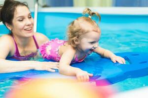 feliz criança Aprendendo para nadar com mãe dentro a piscina foto