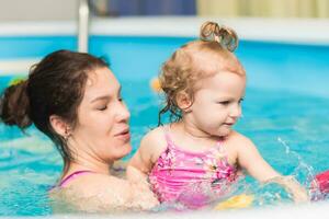 feliz mãe ensina dela pequeno filha para nadar dentro a piscina foto