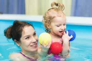 feliz bebê menina nada dentro a piscina com dela mãe foto