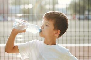 fofa criança bebidas água a partir de uma garrafa em a rua dentro verão foto