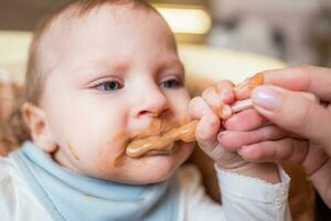 mãe feeds dela pequeno filha fruta purê a partir de uma colher. primeiro Comida foto