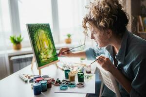 mulher sentado dentro frente do uma pintura e pintura com escovas em tela de pintura às casa foto