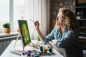 mulher sentado dentro frente do uma pintura e pintura com escovas em tela de pintura às casa foto