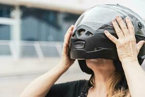 retrato do meio envelhecido Loiras fêmea motociclista colocando Preto capacete em cabeça foto