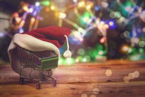 Natal compras x-mas venda conceito. compras carrinho e santa boné contra decorado com festivo luzes Natal árvore. Natal gastos foto