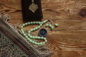 tradicional muçulmano oração conjunto pacote. Rezar tapete, rosário miçangas, pequeno versão do a piedosos Alcorão e qibla bússola em de madeira fundo. livre espaço foto